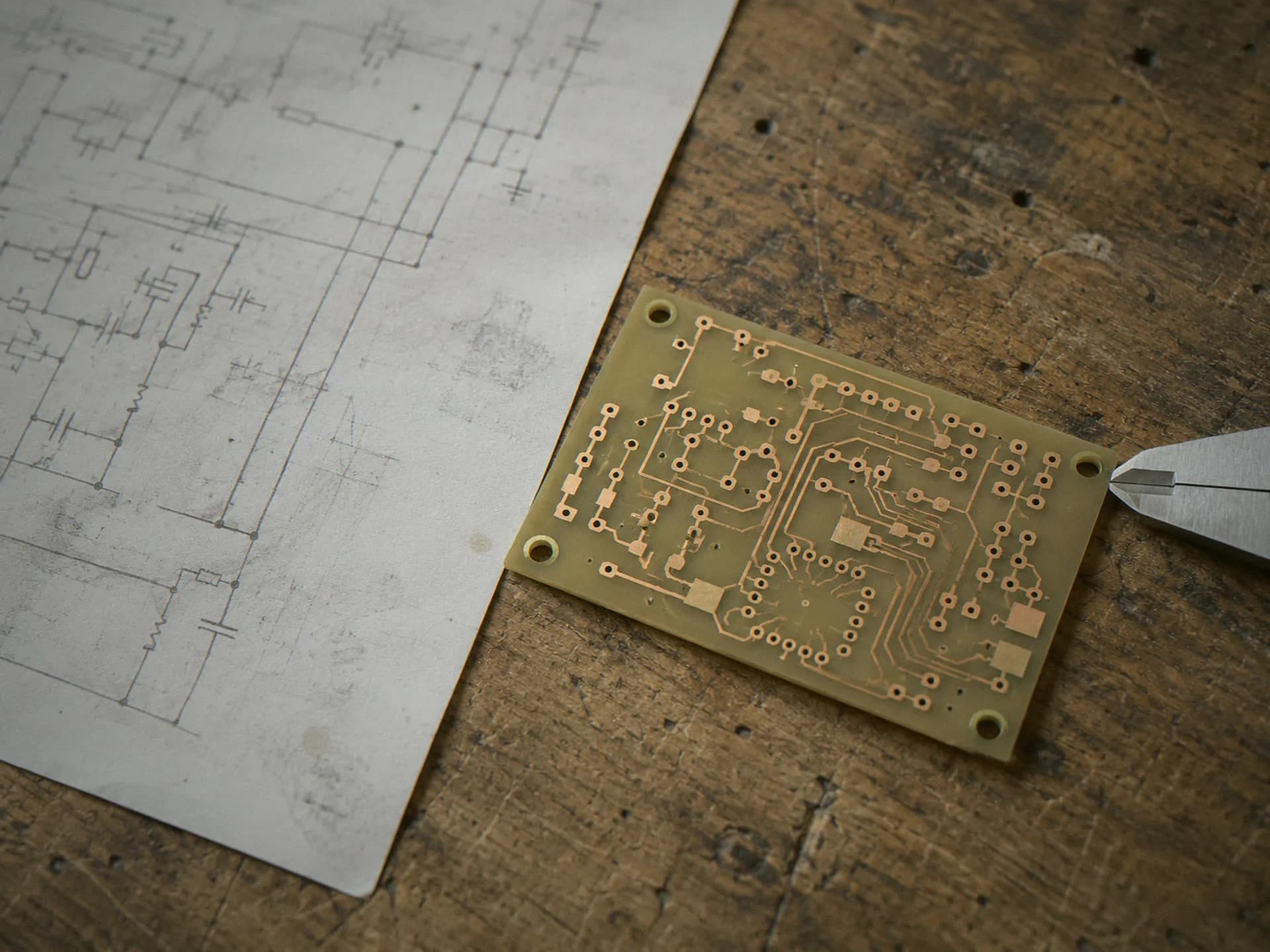 Schematic printout, bare prototype board and calipers on an engineering bench