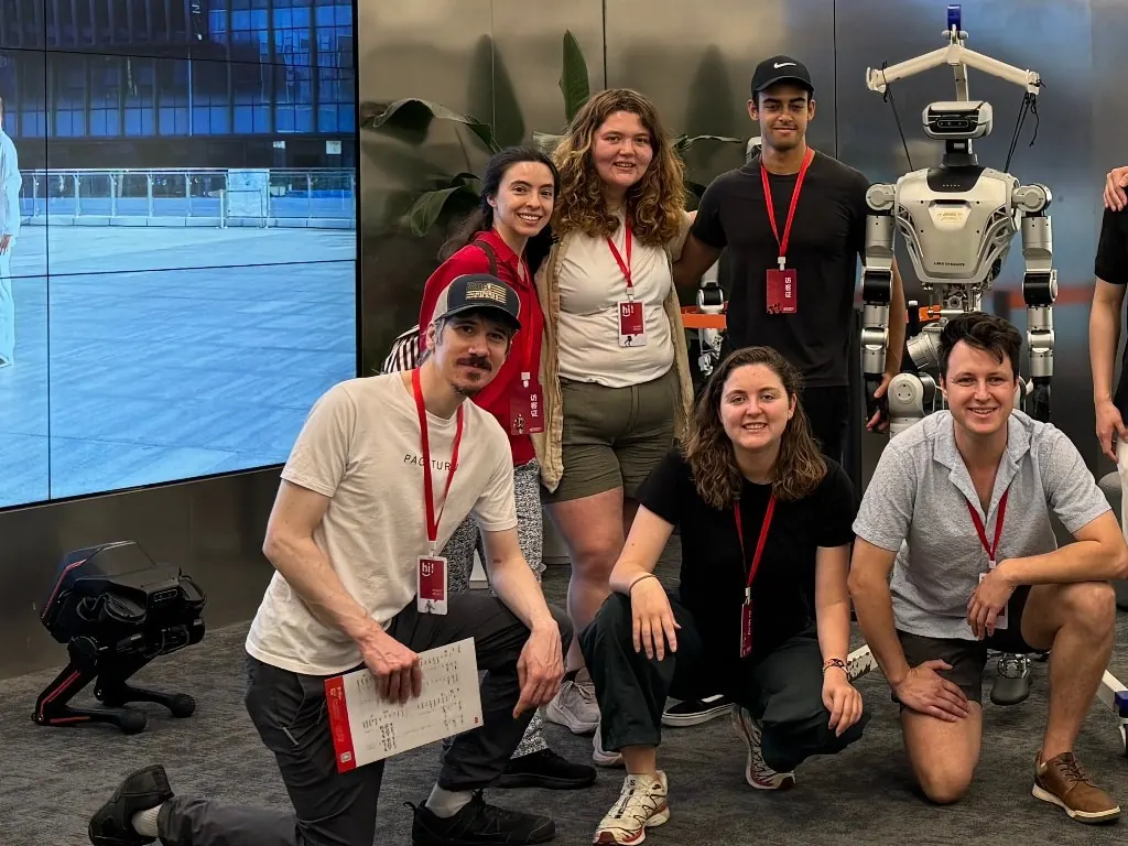 Founders with visitor badges posing with a humanoid robot in a robotics lab