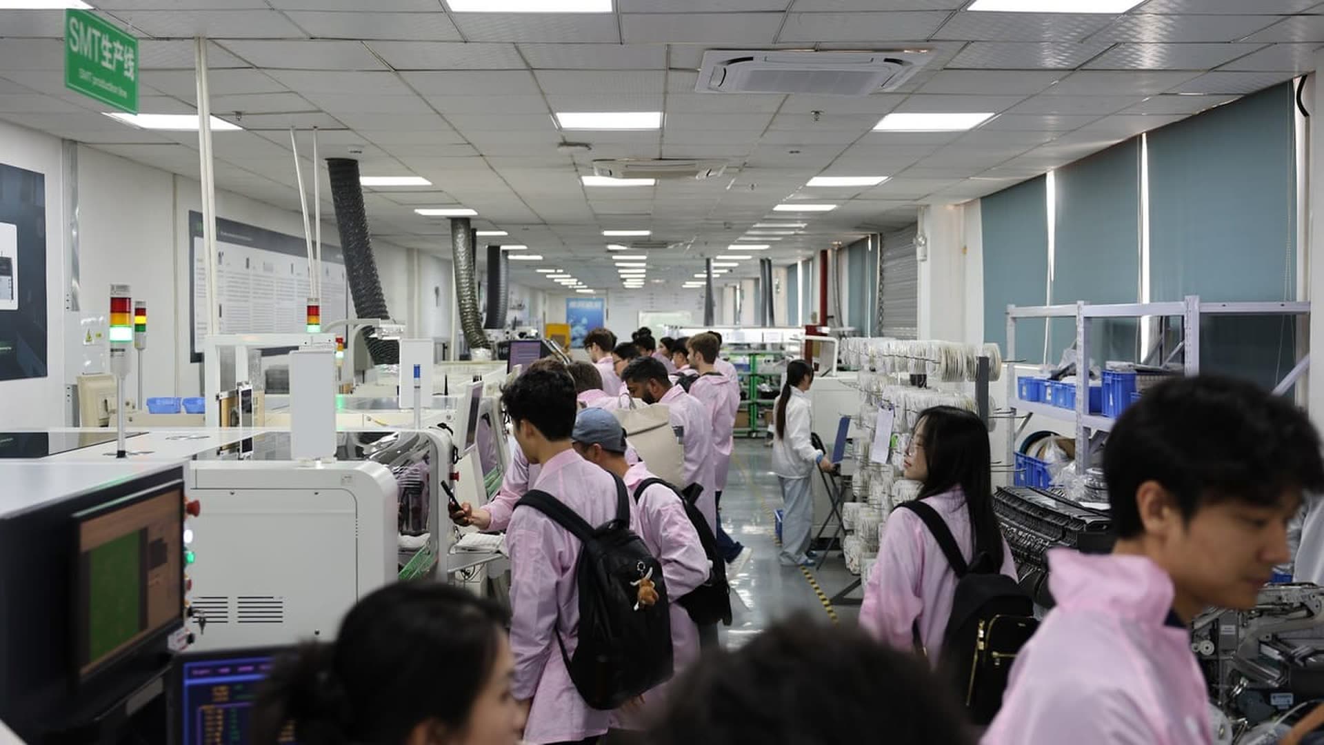 Founders in ESD smocks walking past the machines of an SMT production line
